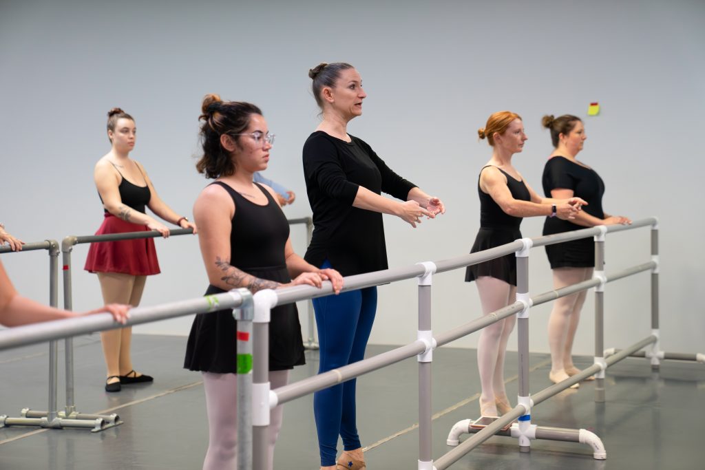 Picture of Anne Carollo teaching an Adult Intro to Ballet Series class.  Here the students are working on their balances at the barre.