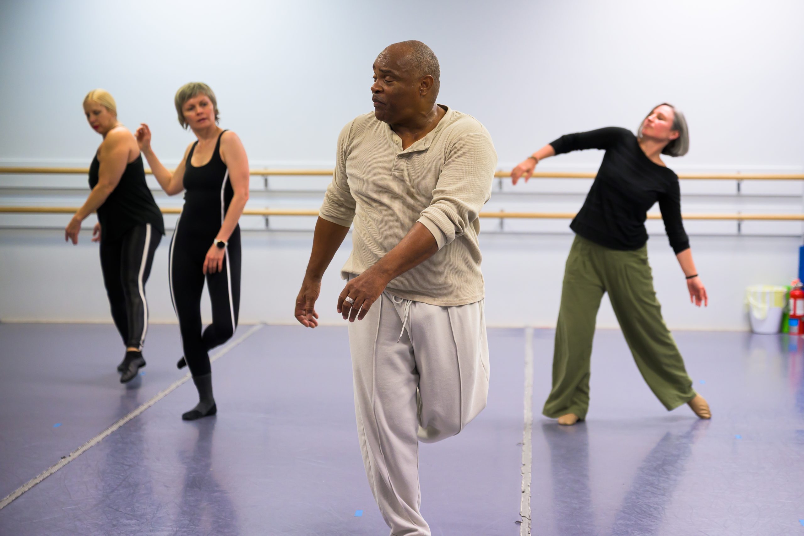Adult dancers at the ballet barre stretching.