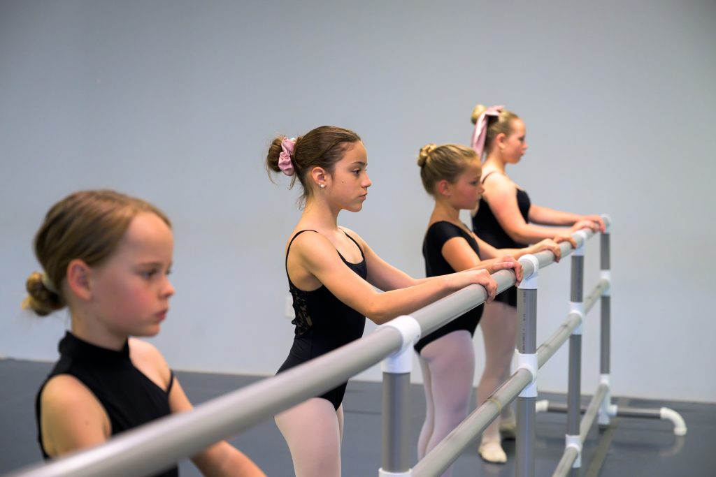 Level 2 ballet students at the barre warming up their bodies at the start of ballet class.